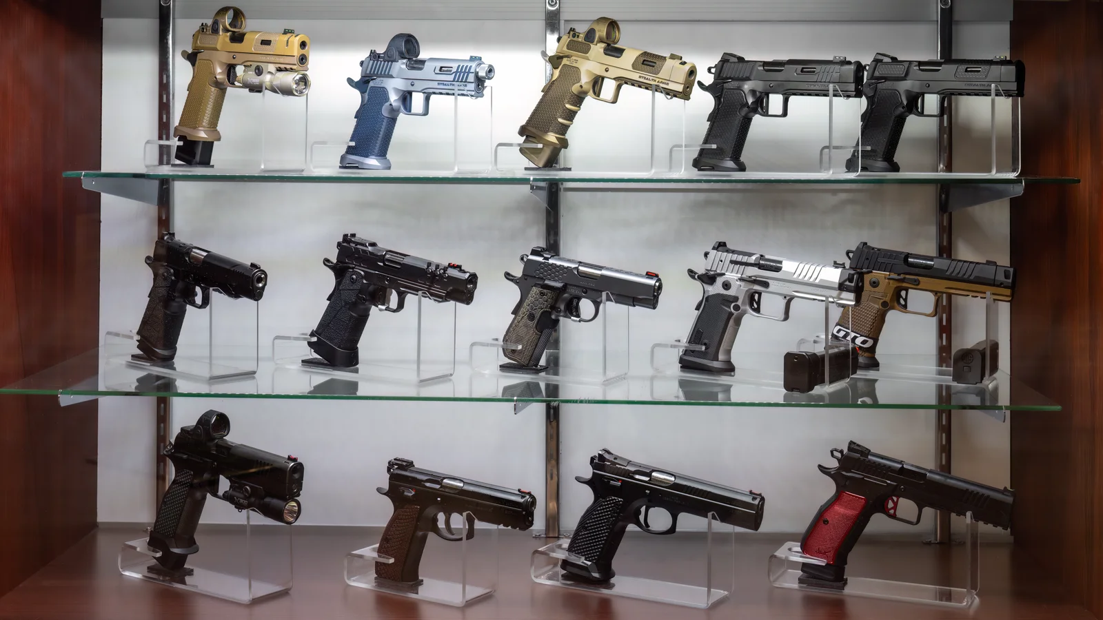 Glass display case of pistols on three shelves under bright light, several with red dot optics