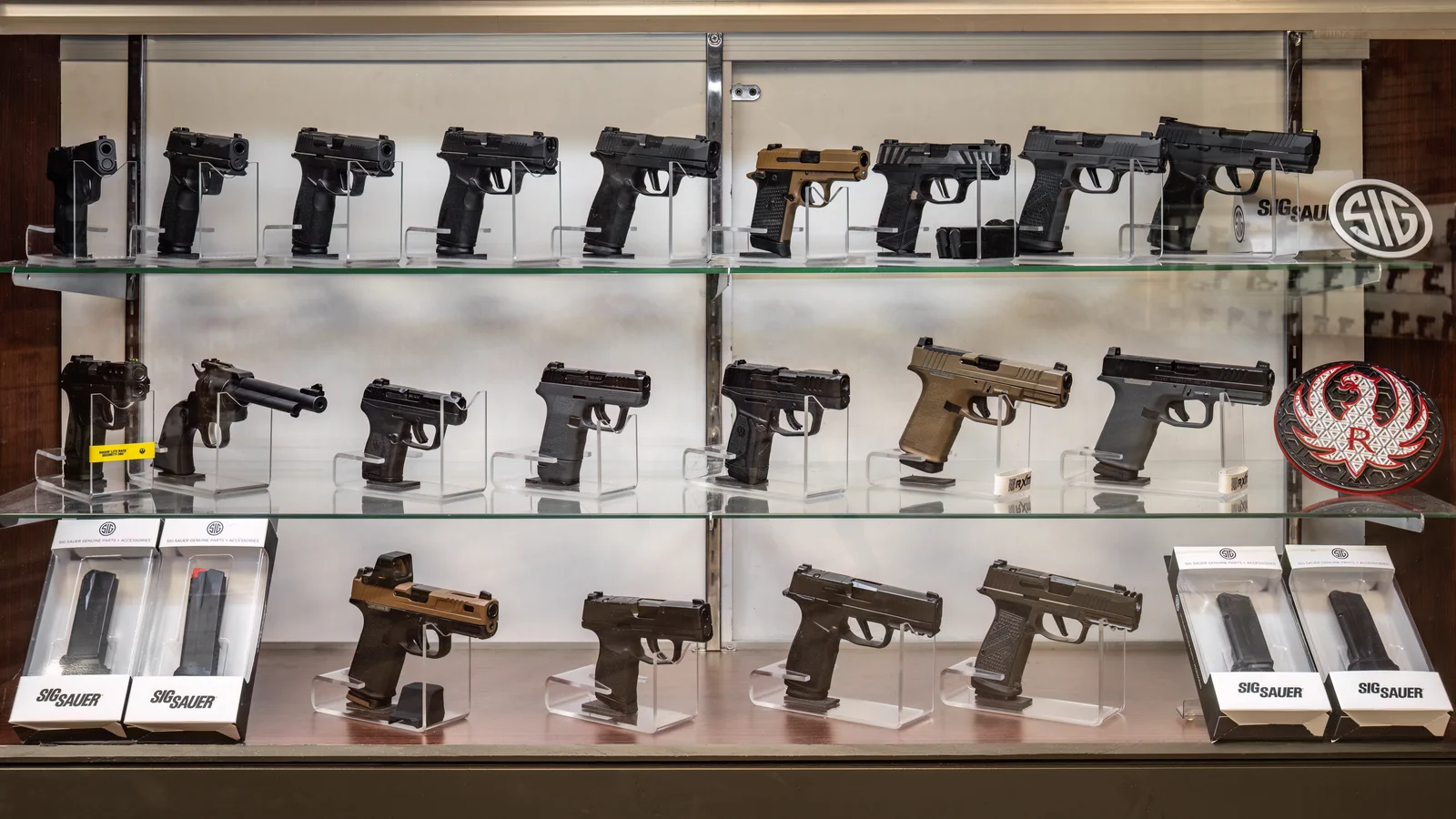 Glass case of pistols on three shelves with Sig Sauer and Ruger logos