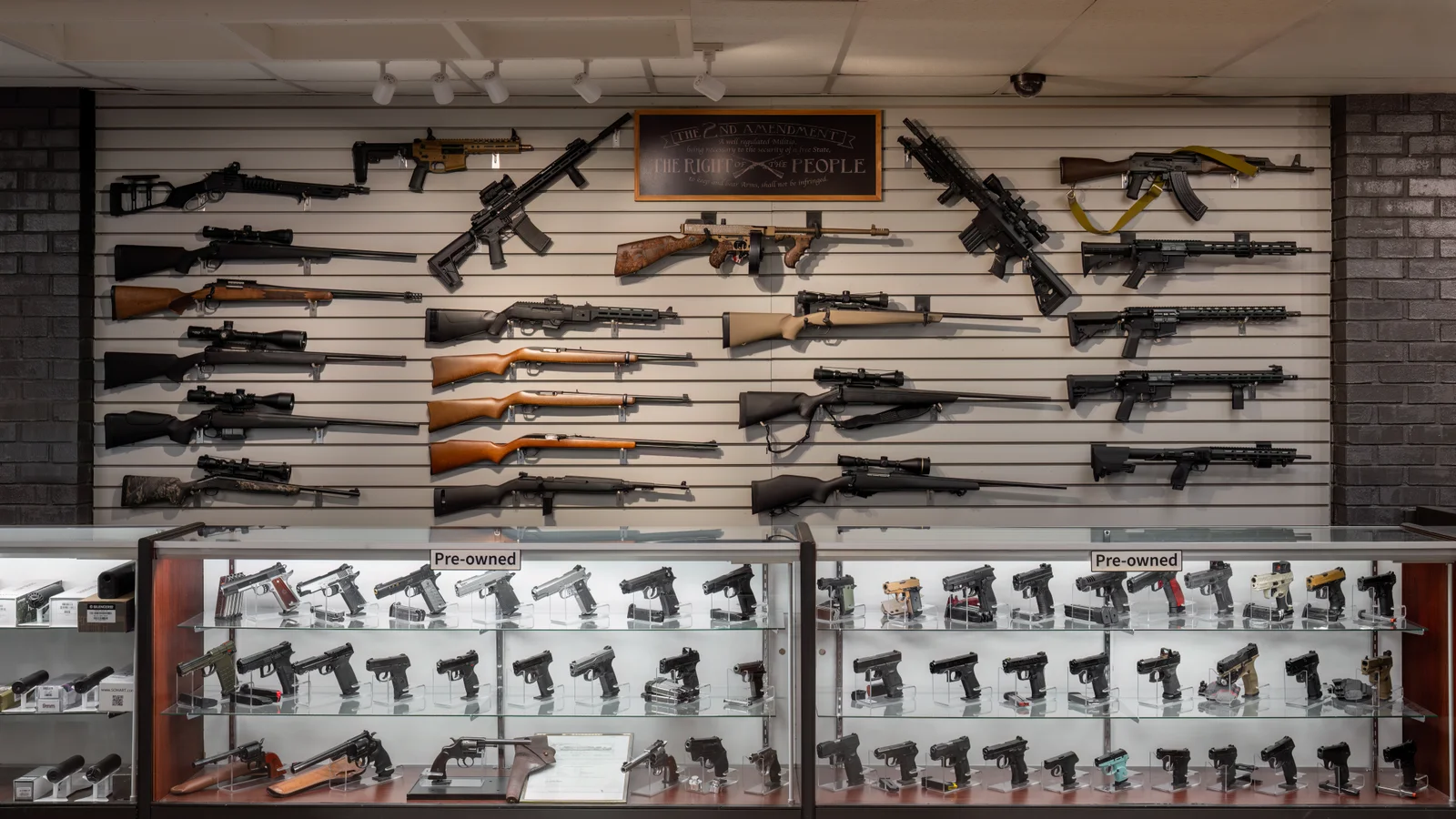 Rifle wall above two glass cases labeled Pre-owned, with a Second Amendment sign on the wall