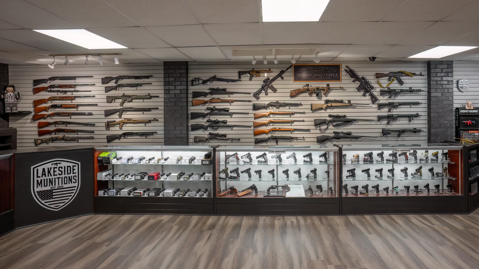 Store corner with a wall of rifles and shotguns above a glass counter, with a Lakeside shield on the counter front