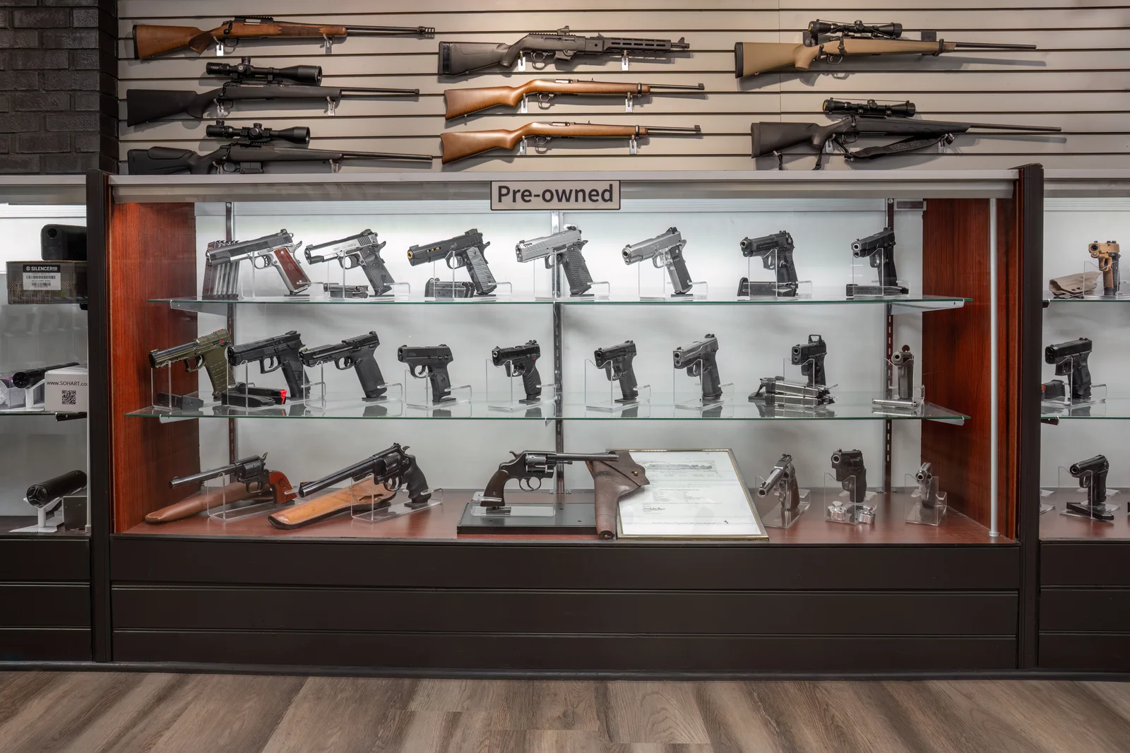 Pre-owned glass case of handguns on three shelves under a wall of rifles
