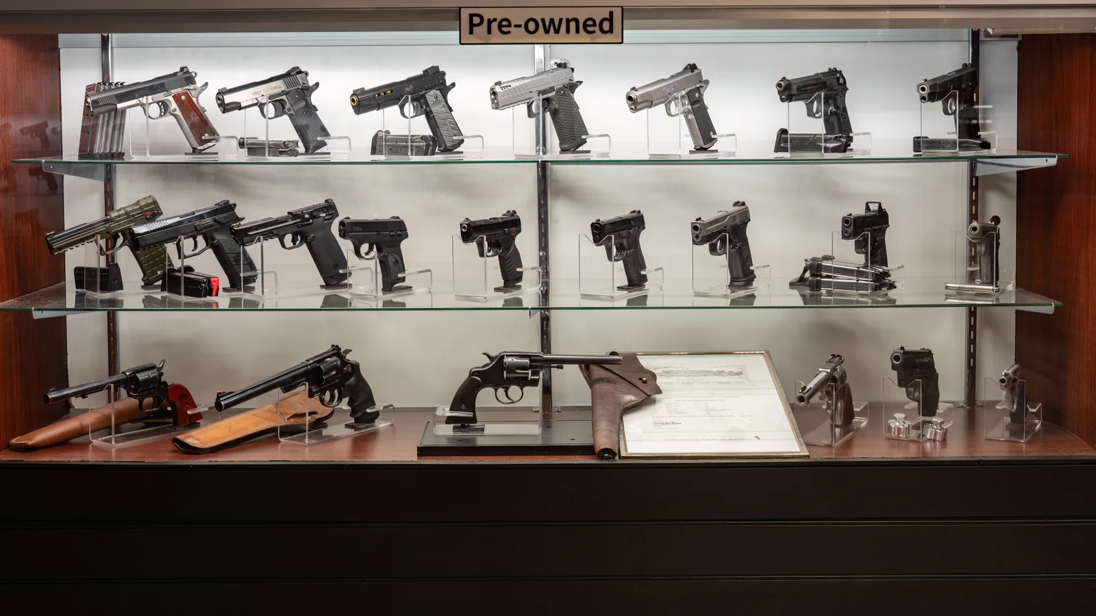 Pre-owned glass case with revolvers, a framed document and pistols on three shelves