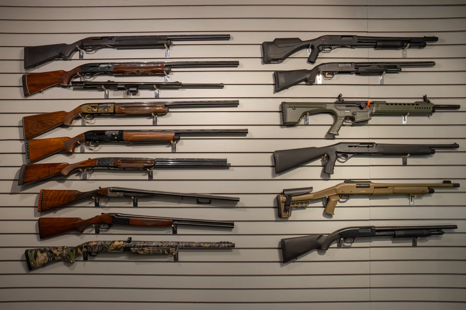 Slatwall of shotguns with wood, camo and black stocks hung in rows