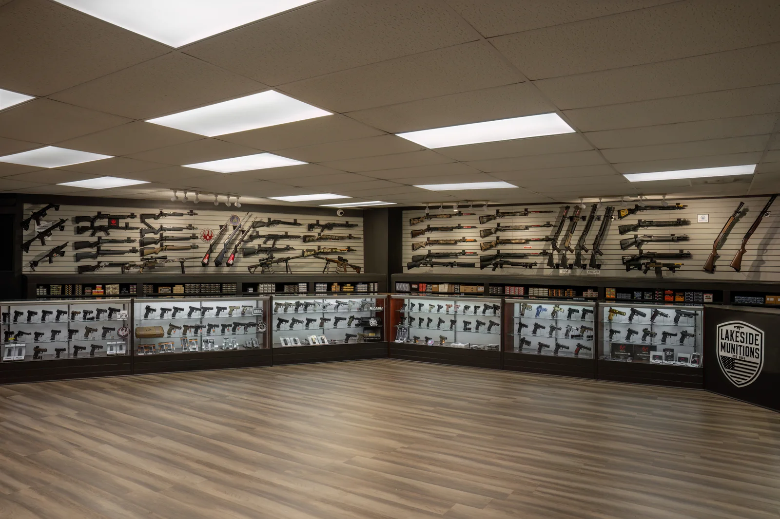 Wide showroom with glass handgun cases along the walls, a Lakeside shield on a dark divider, and rifles above