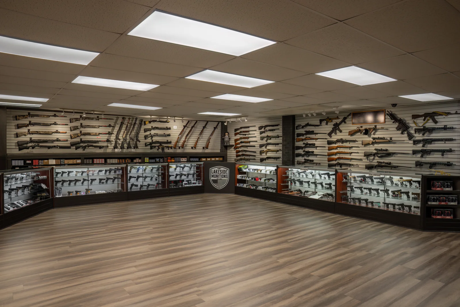 Wide showroom with curved glass handgun cases, a Lakeside shield on the end panel and rifles above