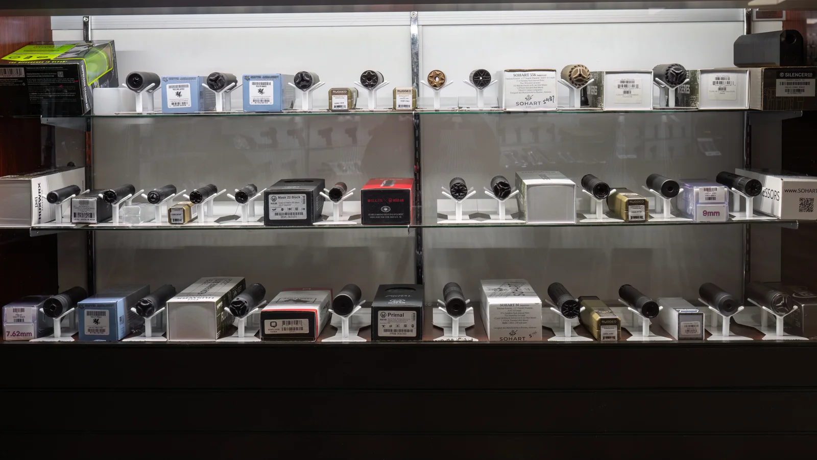 Glass case of suppressors on white stands across three shelves